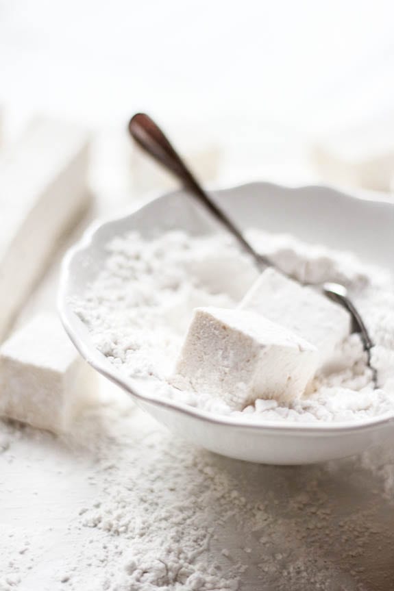 Marshmallows in a bowl of powdered sugar with a spoon