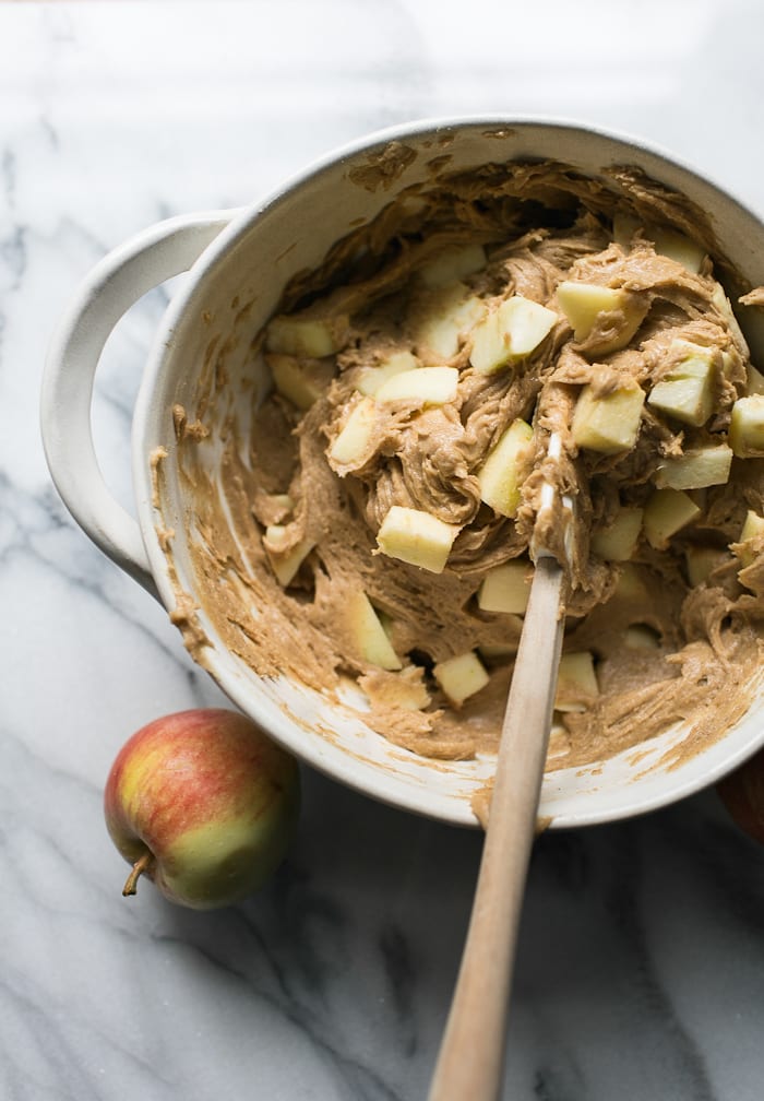 Bowl of apple cake batter with chunks of apples and a white spatula