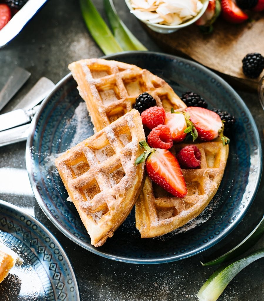 Cinnamon sugar sourdough waffles with fresh fruit on a blue plate.