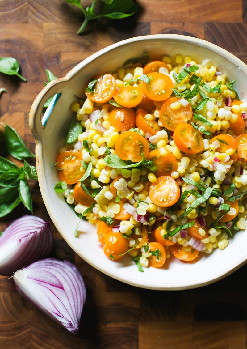 Bowl of fresh corn, halved orange sun gold tomatoes, red onion and basil.