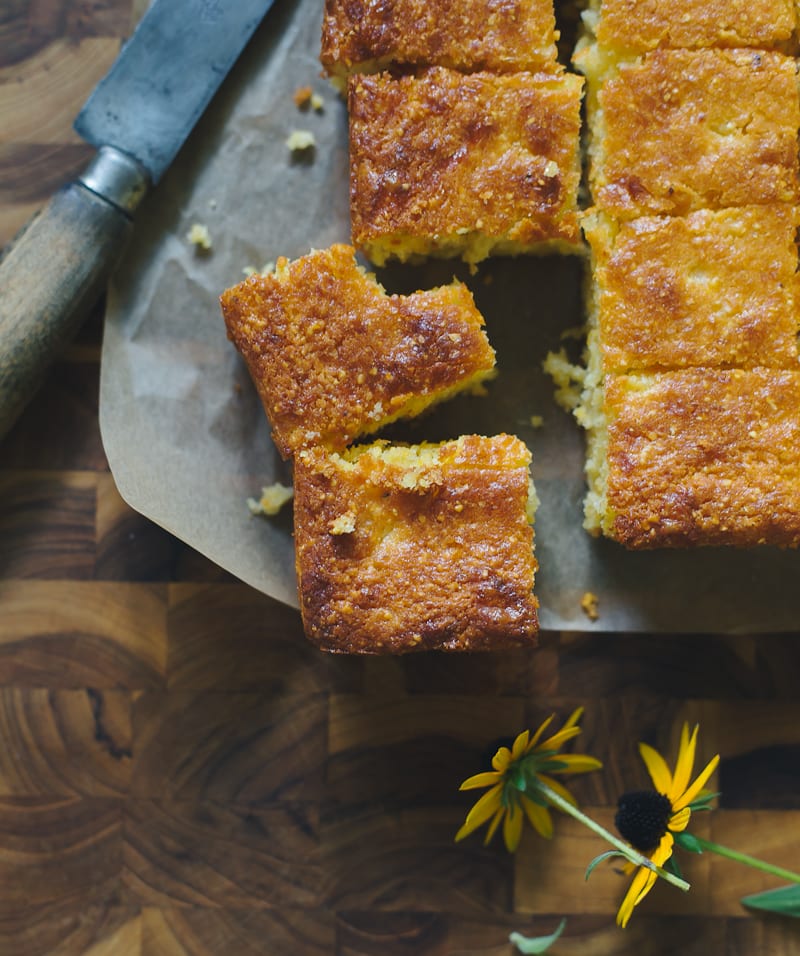 Close up of sourdough cornbread thick cut squares on a cutting board with crumbs