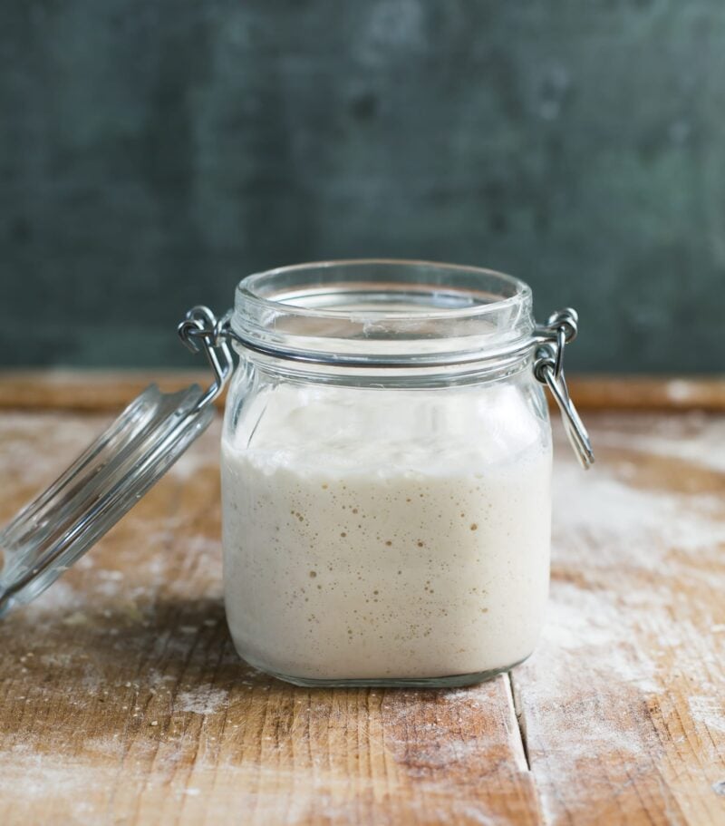 Jar of fed, active sourdough starter that has doubled in size, at peak height, on a wooden surface