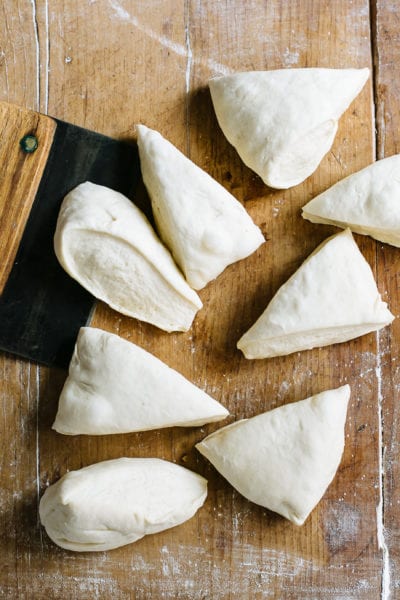 Sourdough bagel dough, cut into wedges with a bench knife, on a wood surface.