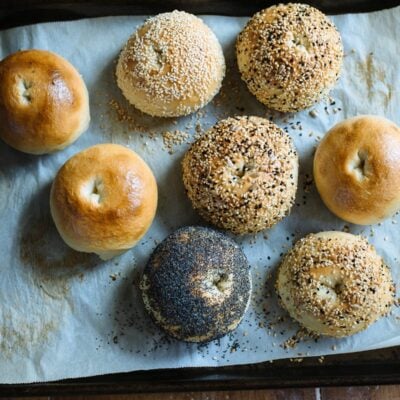 Homemade sourdough bagels with mixed toppings on a parchment-lined sheet pan