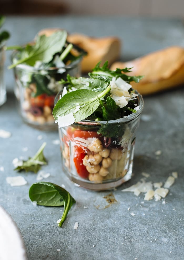 Kale salad with chickpeas, tomatoes and olives in small individual jars.