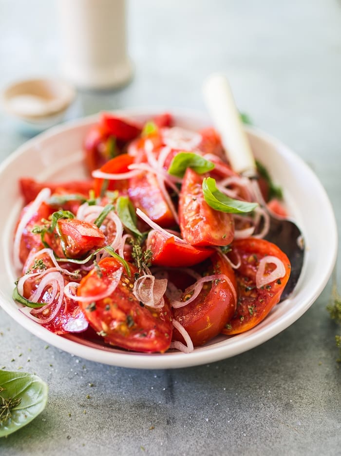 Bowl of juicy red tomato wedges with shaved onion and herbs.