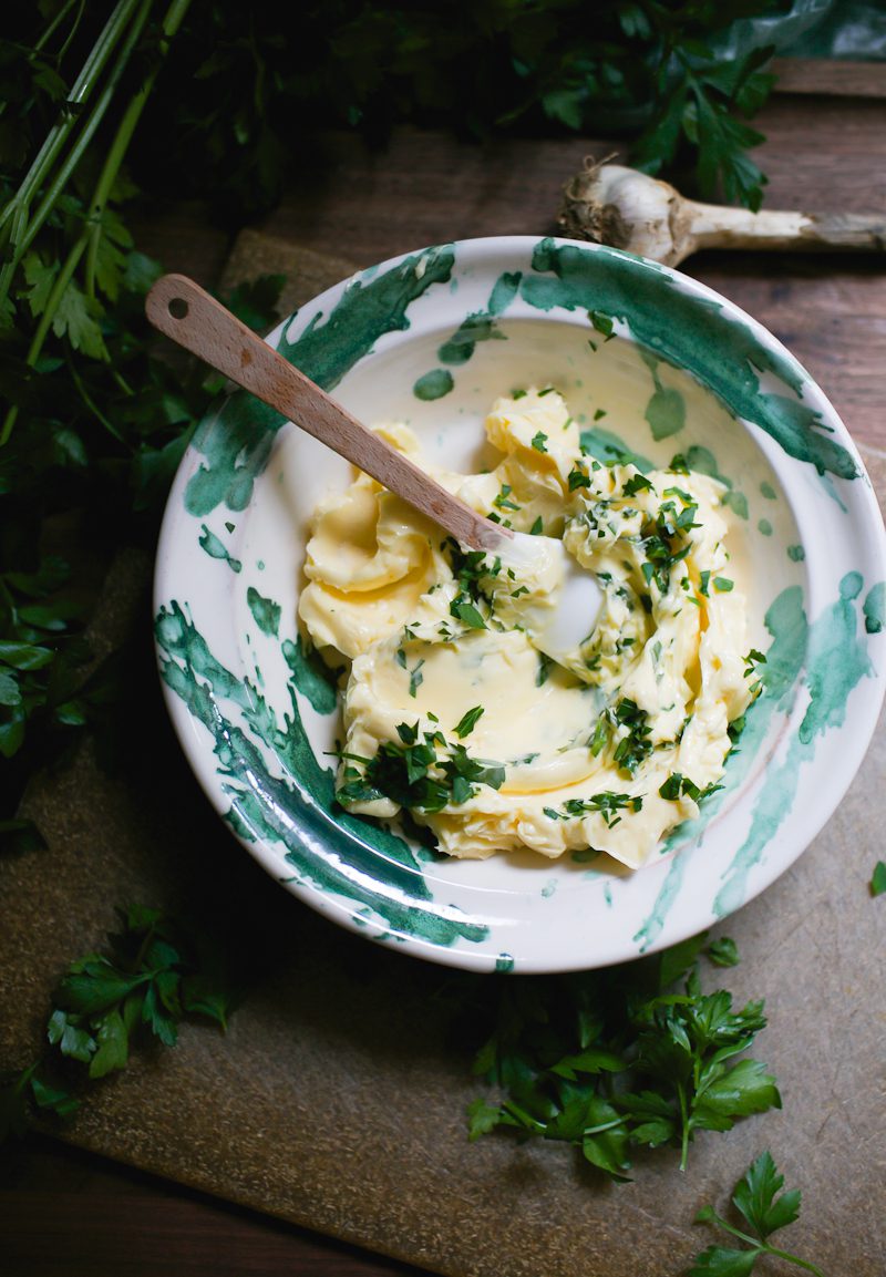 Green and white bowl with softened garlic butter with parsley.