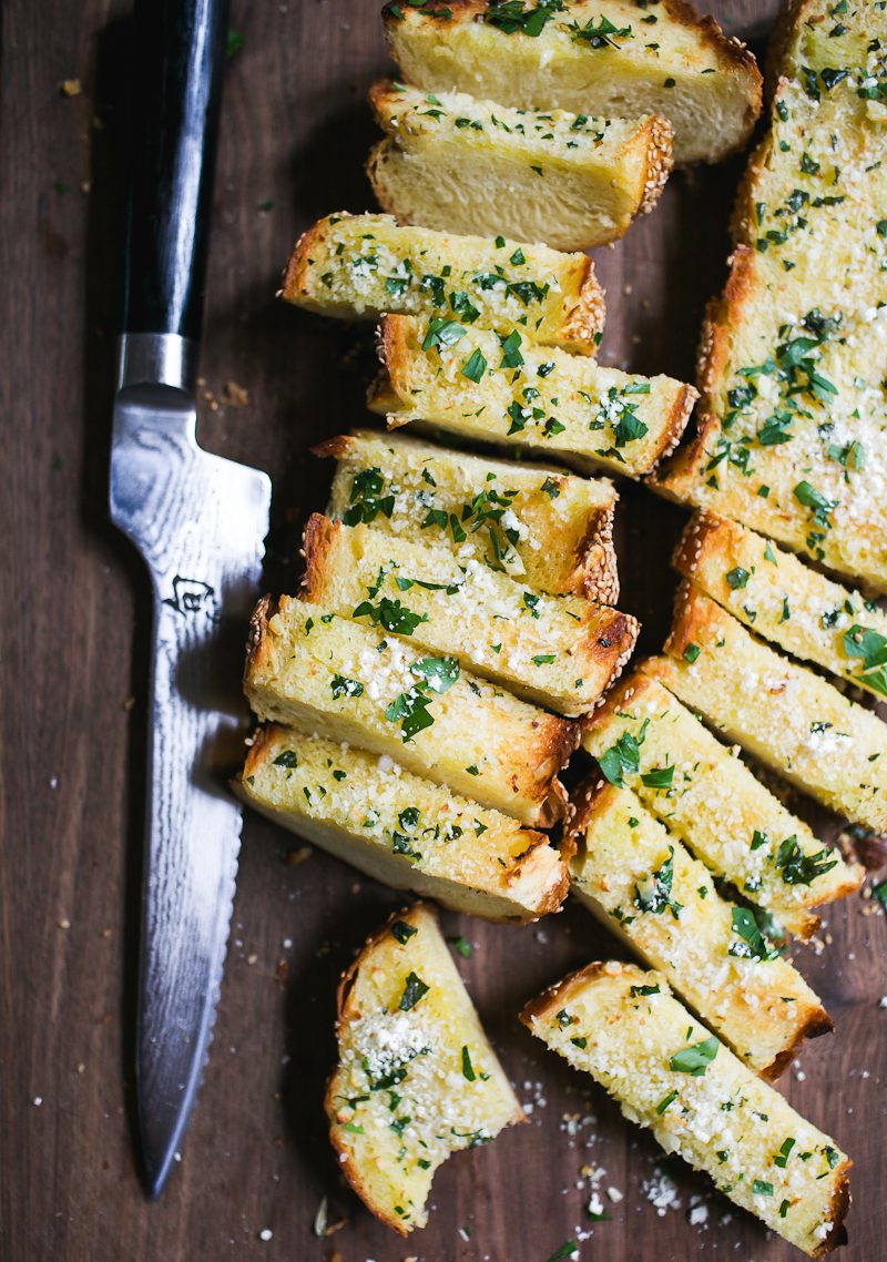 Cut slices of garlic bread on a wooden cutting board with a serrated knife.