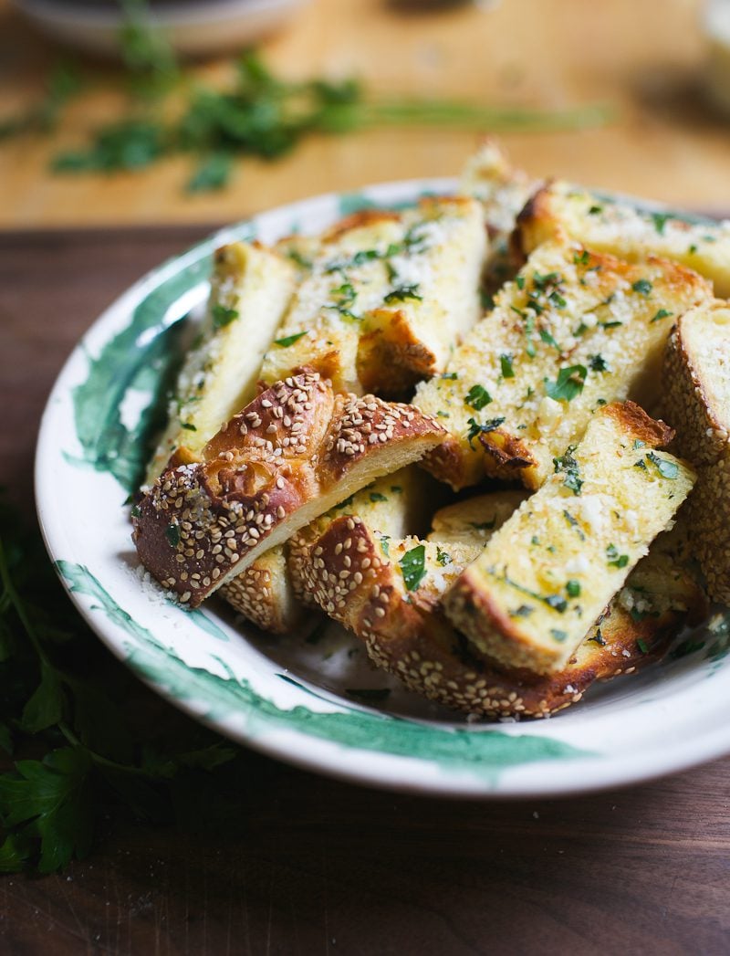 Green and white bowl with cut garlic bread slices with sesame seeds.