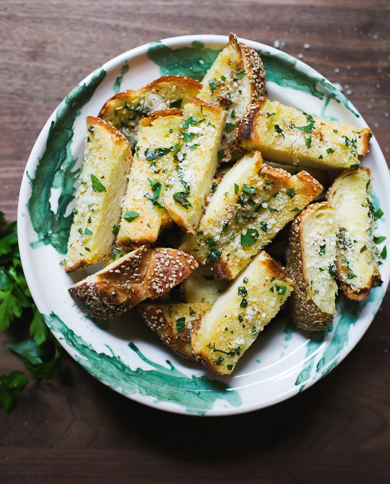 Green and white bowl with sliced garlic bread with sesame seeds.