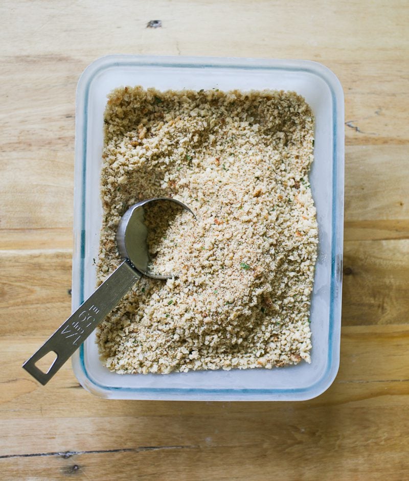 Seasoned sourdough breadcrumbs in a rectangular baking dish with a measuring scoop