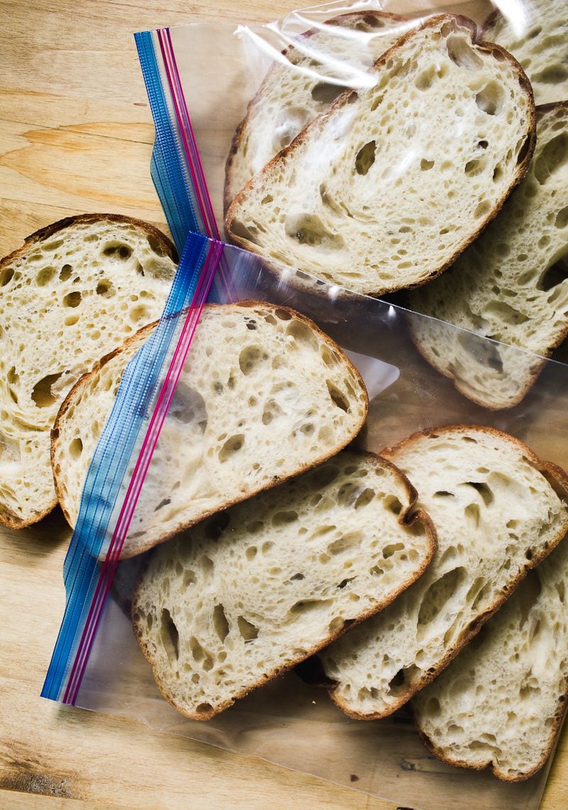 Slices of sourdough bread in a zip-top bag, on top of a cutting board, ready to go in the freezer.