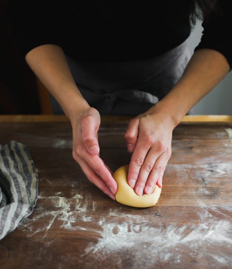 A hand flattening a piece of fresh pasta dough into an oval shape