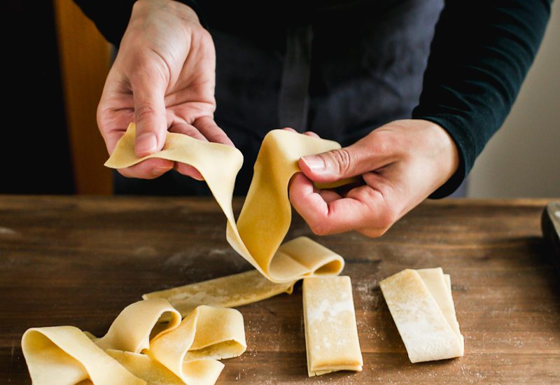 Separating cut homemade pasta dough sections into pappardelle noodles