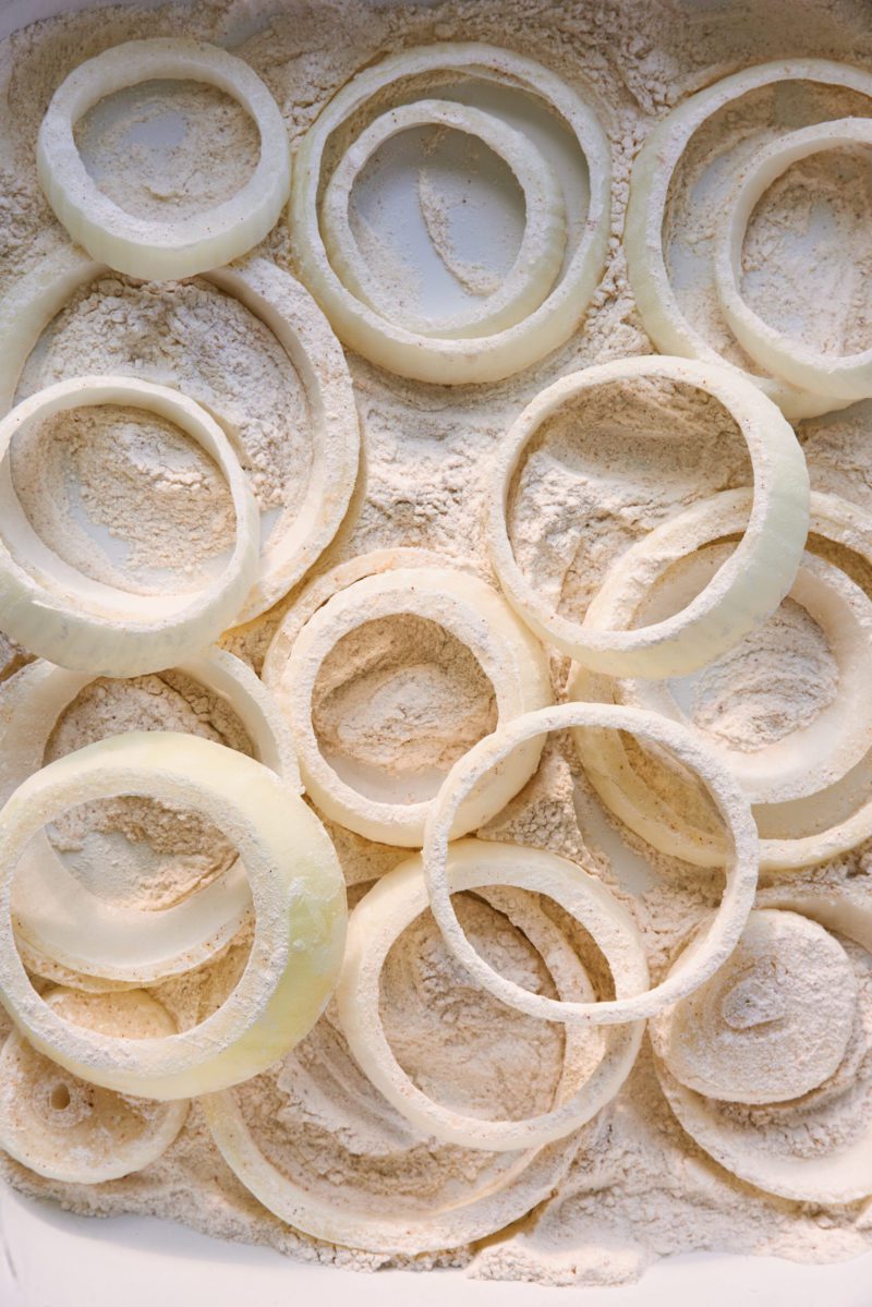 A white tray of flour coated onion ring slices