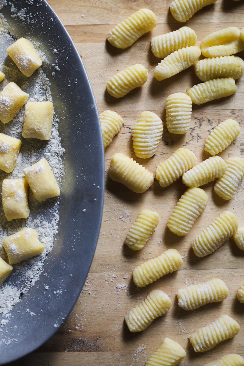 Fresh homemade potato gnocchi on a wooden cutting board and oval sheet pan.