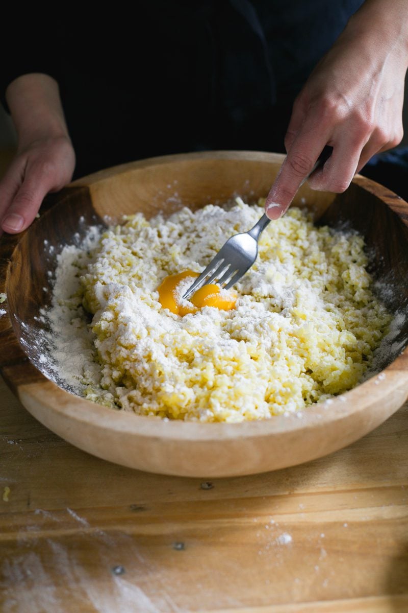 Mixing riced potatoes, salt, flour and egg yolk with a fork in a wooden bowl.