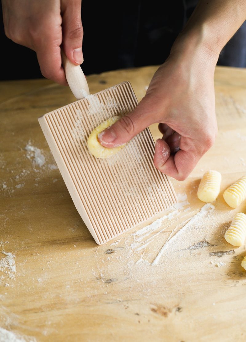 Hand rolling gnocchi on a wooden gnocchi board.