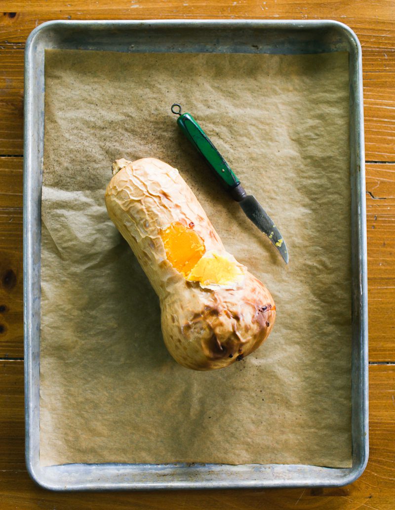 Whole-roasted butternut squash on a parchment-lined sheet pan with a small knife