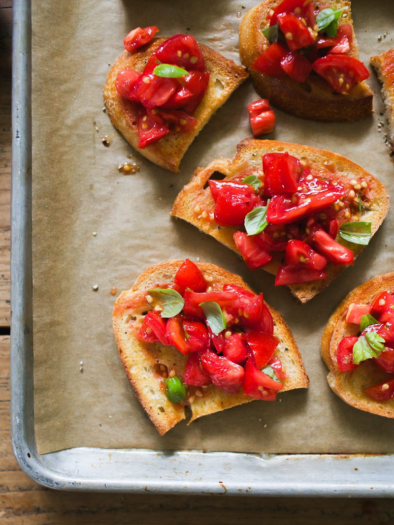 Sourdough bruschetta with tomatoes and basil on a parchment lined sheet pan