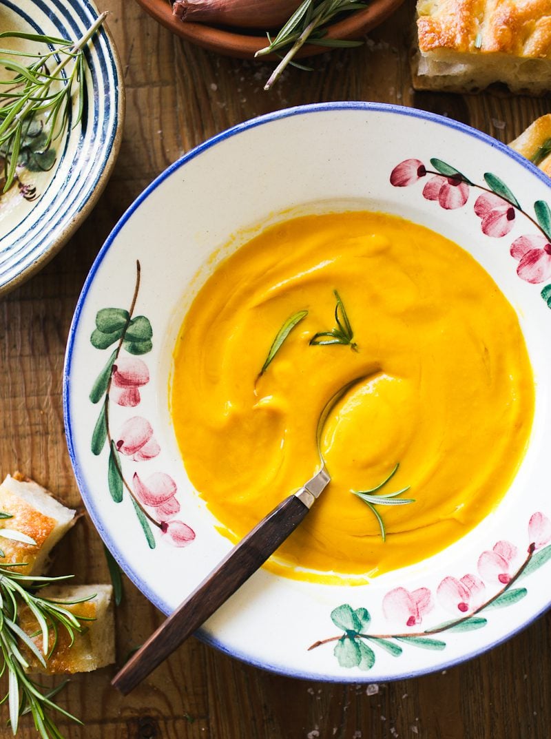 Creamy butternut squash soup in a bowl with flowers and green sprigs.
