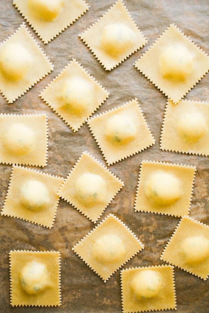 Fresh homemade ravioli with cheese filling on a parchment-lined sheet pan