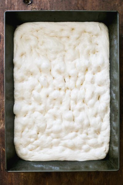 Dimpled sourdough pizza dough in a non-stick baking pan
