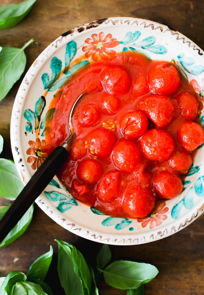 Bowl of canned cherry tomatoes on a wooden board with fresh basil leaves