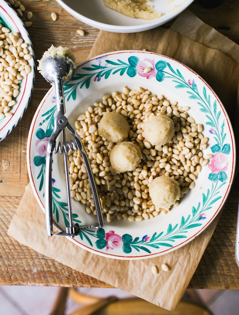 Pignoli cookie dough balls in a bowl of pine nuts