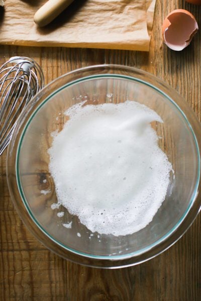 Frothy egg whites in a large bowl with a whisk