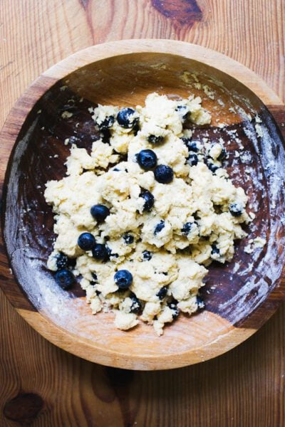 Dry ingredients & wet ingredients mixed together in a wooden bowl w/ fresh blueberries