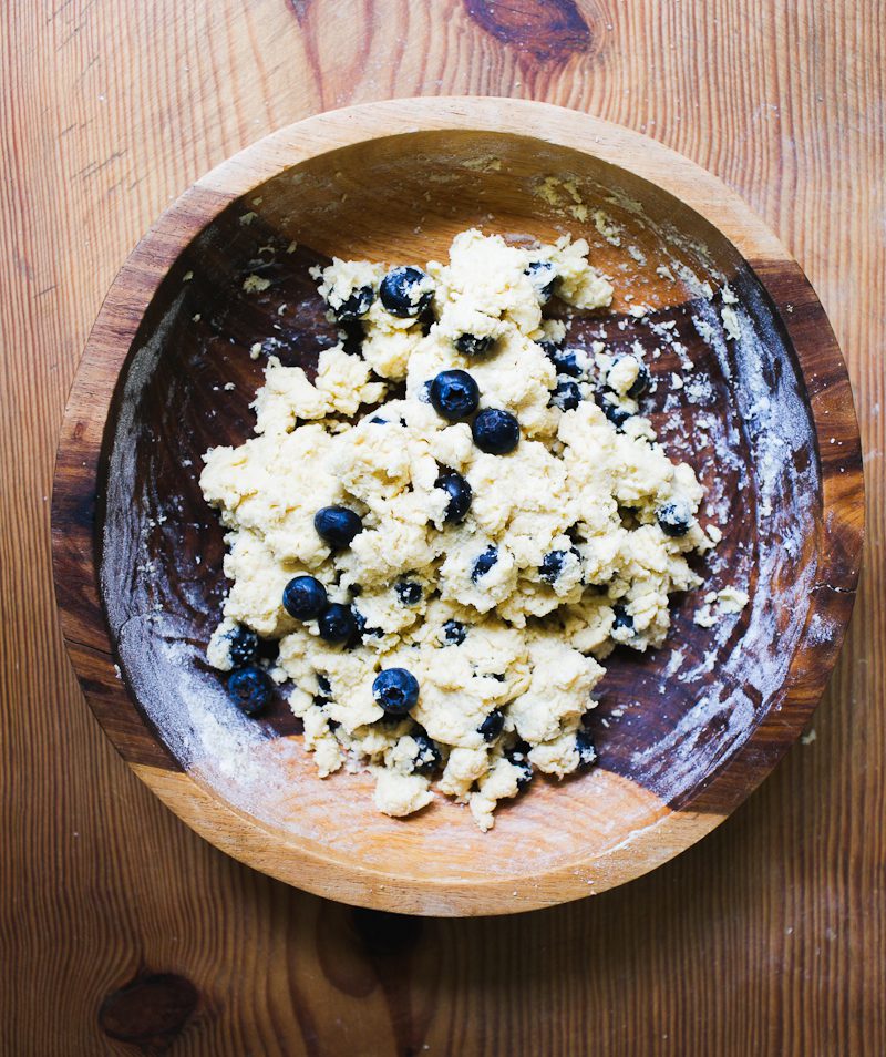 Dry ingredients & wet ingredients mixed together in a wooden bowl w/ fresh blueberries