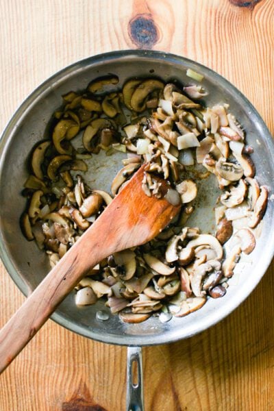 Sautéed sliced mushrooms, shallots, garlic and marsala wine in a large skillet with a wooden spoon