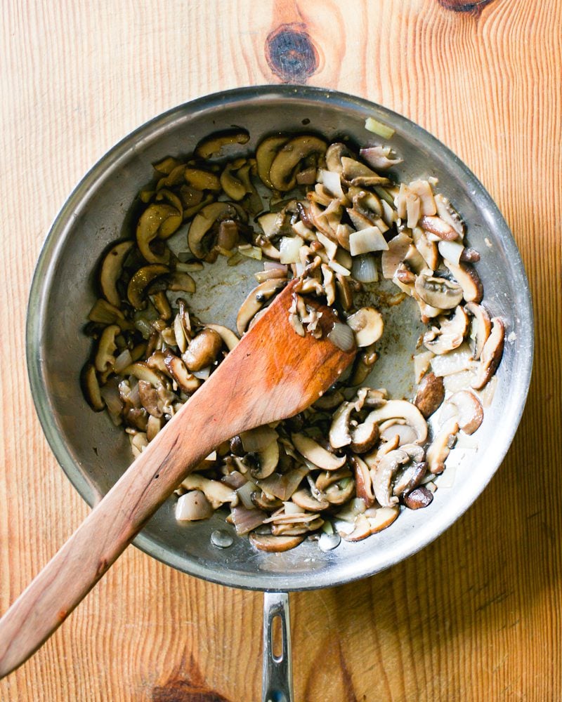 Sautéed sliced mushrooms, shallots, garlic and marsala wine in a large skillet with a wooden spoon
