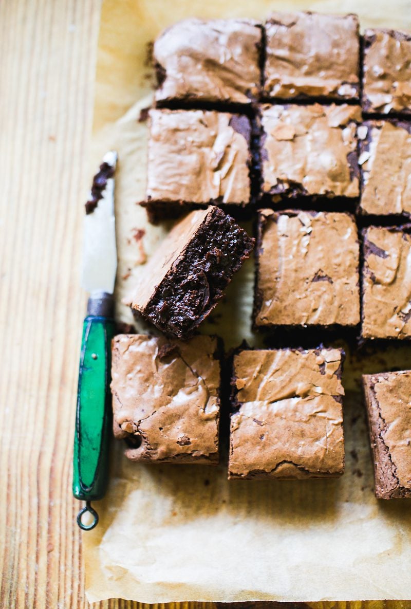 Fudgy, sourdough brownies cut into thick slices on a parchment-lined wooden board with a small, vintage green knife.