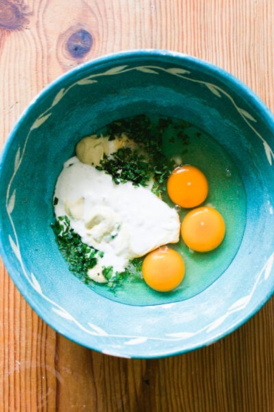 Eggs, sourdough starter, mustard, parsley and spices in a blue mixing bowl