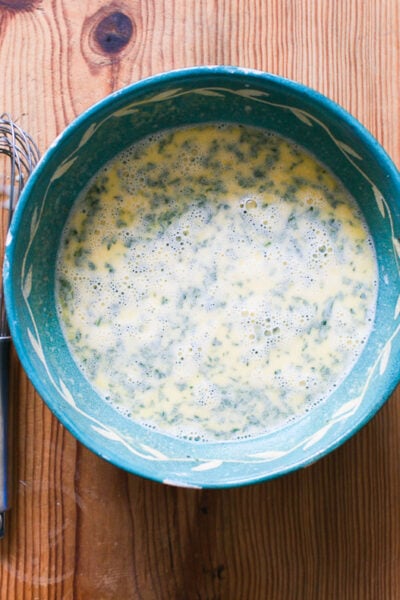 Whisked frothy eggs, sourdough starter, mustard, parsley, spices and warm milk mixture in a blue mixing bowl