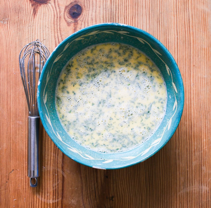 Whisked frothy eggs, sourdough starter, mustard, parsley, spices and warm milk mixture in a blue mixing bowl