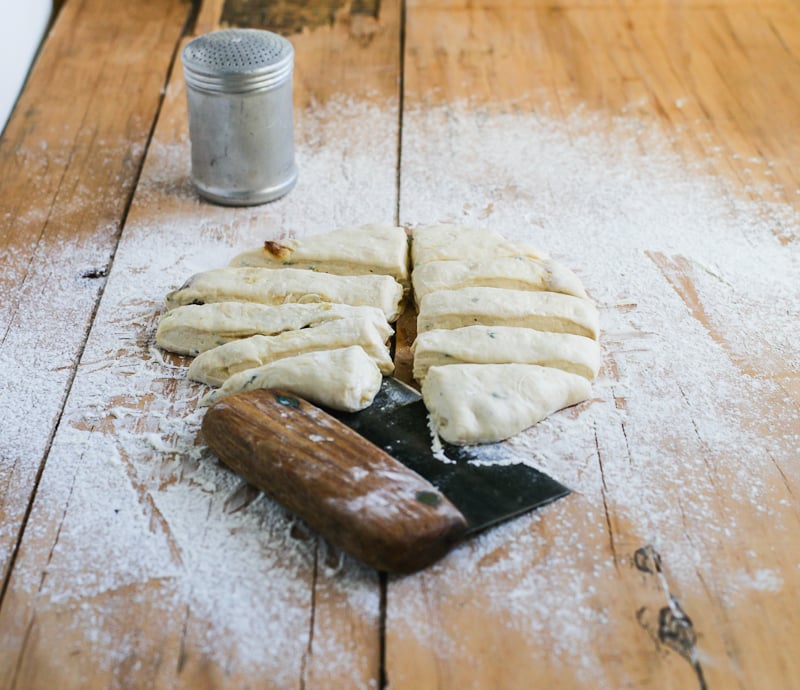 Sourdough garlic knot dough on a floured, wooden surface cut into 10 strips