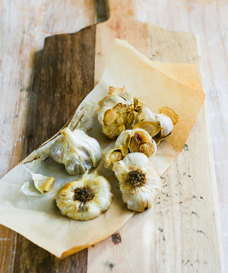 Whole-roasted garlic cloves on a wooden cutting board