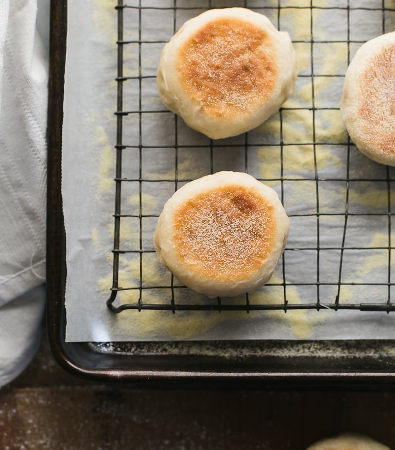 Sourdough English muffins on a vintage wire rack with a white linen tea towel.