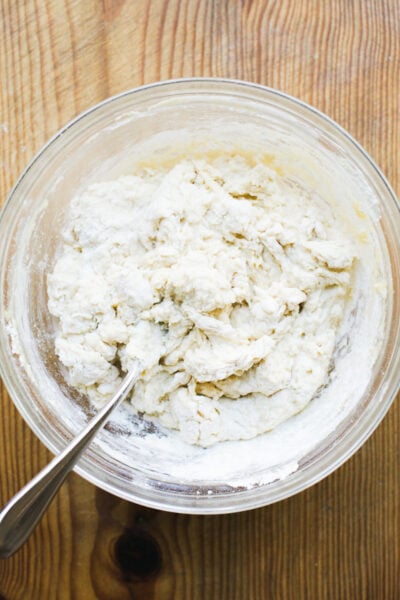 Glass mixing bowl with rough and shaggy dough mixed together with a fork
