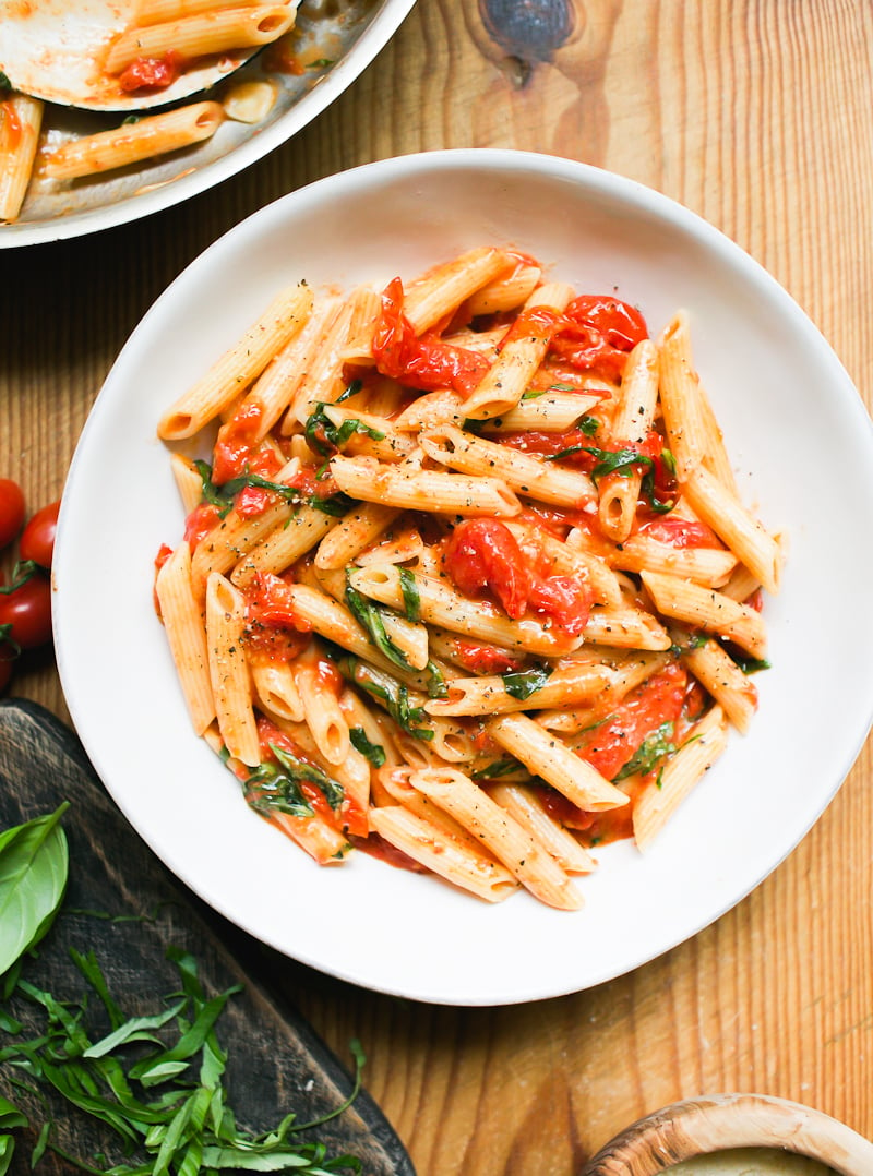 Penne pasta with burst cherry tomato sauce and fresh basil in a white bowl