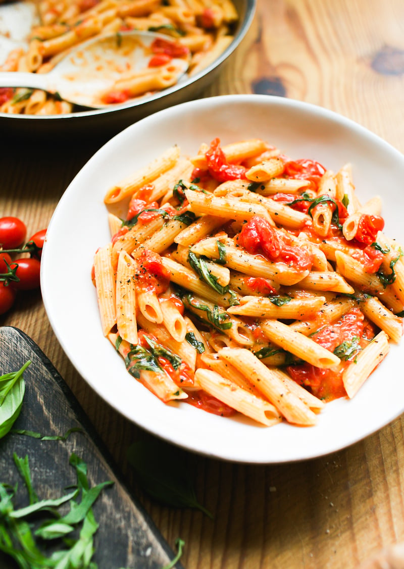 Penne pasta with burst cherry tomato sauce and fresh basil in a white bowl