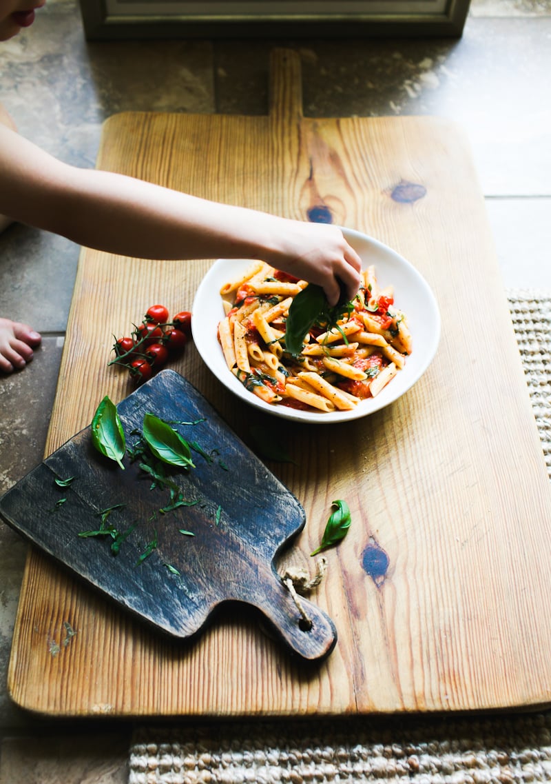 Behind the scenes food photography set up: wooden board on the floor with a bowl of penne pasta with cherry tomato basil sauce
