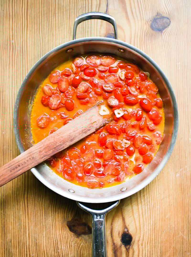 Cooked cherry tomato sauce in a stainless steel pan with a wooden spoon for stirring.