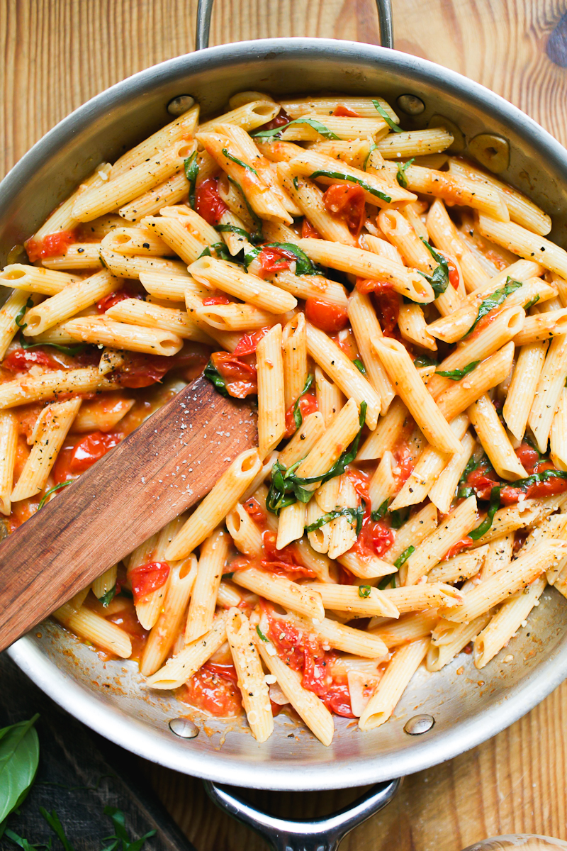 Penne pasta with burst cherry tomato sauce and fresh basil in a pan