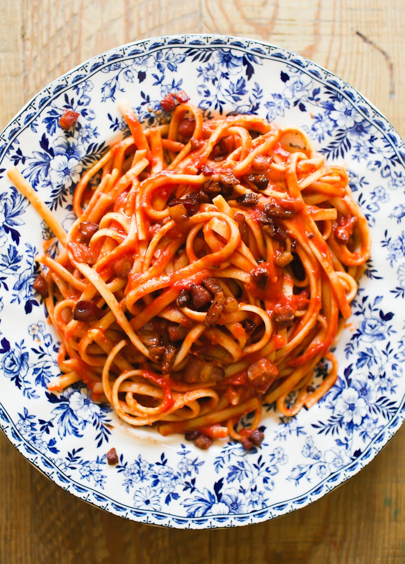 Pasta all"Amatriciana with crispy guanciale on a white and blue plate.