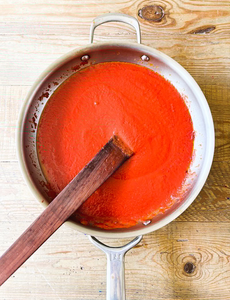 Tomato passata, with sautéed guancial drippings, in a large stainless steel pan with a wooden spoon for stirring.