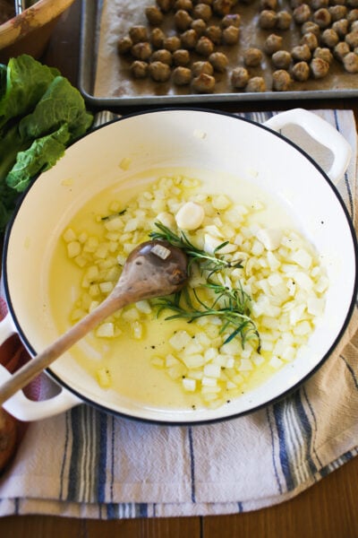 Sautéed onions, garlic, fresh bay leaves and rosemary in a white soup pot.